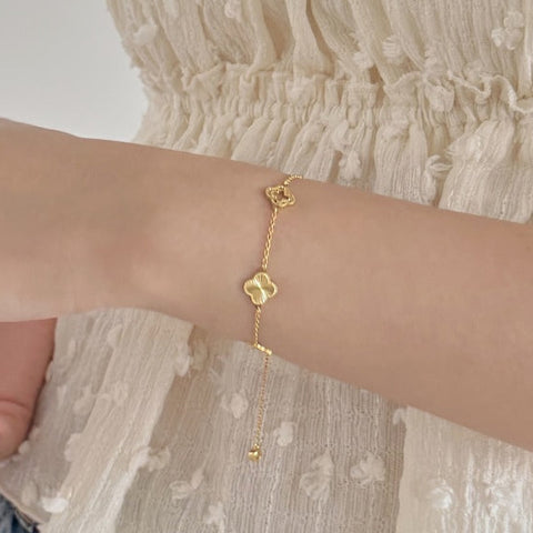 Person wearing a gold bracelet holding a glass against a neutral background