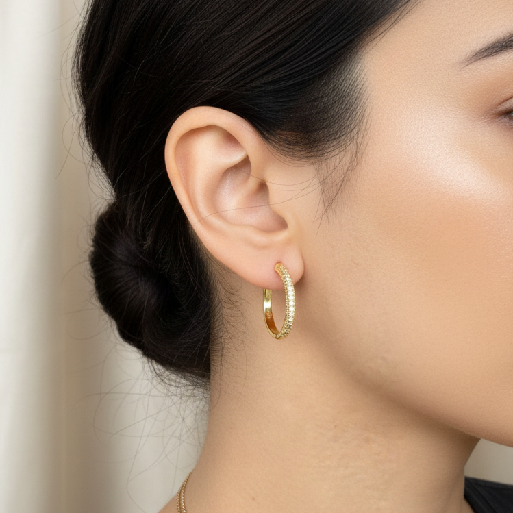 Close-up of a person wearing gold hoop earrings with a neutral background