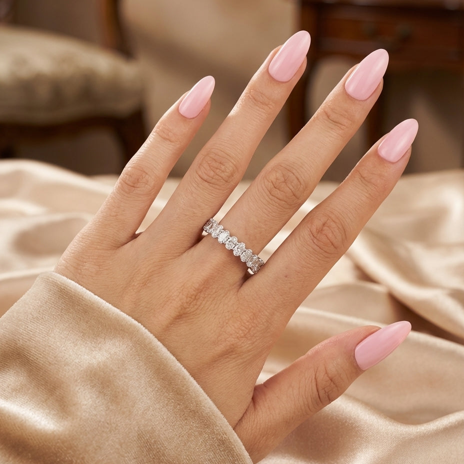 Hand wearing a diamond ring with pink nail polish on a soft fabric background